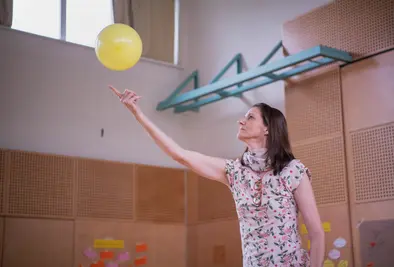 Eine Person streckt ihren Zeigefinger nach einem fallenden Luftballon.