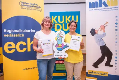 Teilnehmende Person posieren mit Zertifikat und KUKUDU Logo.