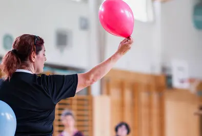 Eine Person hält zwei Luftballons in beiden Händen und spricht zu den Teilnehmenden.