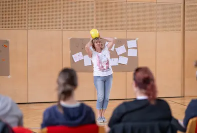 Vortragende steht mit einem Luftballon auf dem Kopf vor den Teilnehmenden. 
